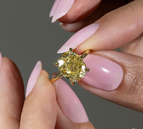 A woman holds a rare elongated cushion cut yellow diamond engagement ring.