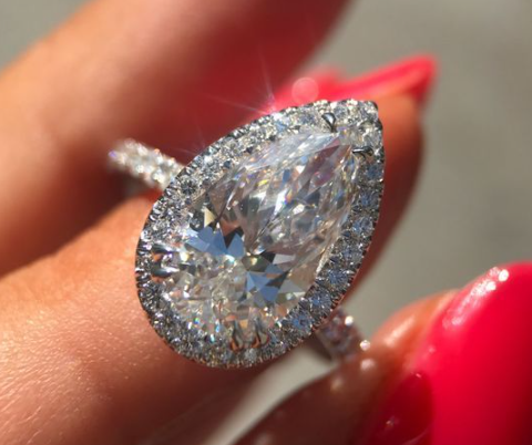 A woman holds a pear-shaped diamond engagement ring with a diamond that looks bigger.