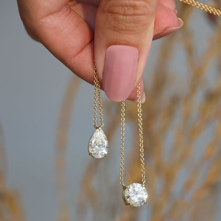 A woman holds a Round Shaped and a Pear Shaped Diamond Pendant on a Yellow Gold chain. These are two of the best shapes for Diamond Pendants.